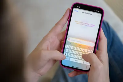 En person håller en iPhone med en Genmoji-app öppen. Tangentbordet är synligt.