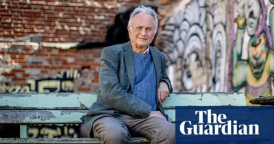 Richard Dawkins sitter på en bänk framför en vägg med graffiti. Han bär kavaj och tröja. Logotypen för The Guardian syns.