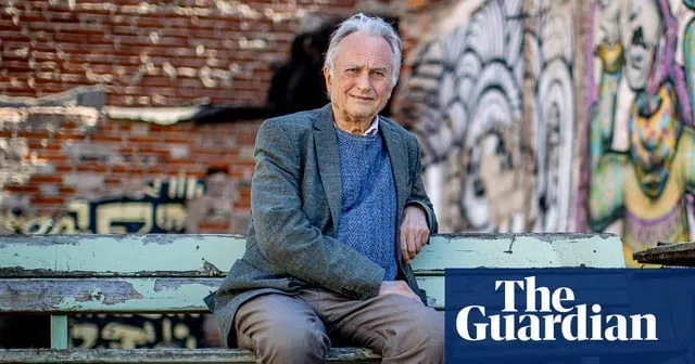 Richard Dawkins sitter på en bänk framför en vägg med graffiti. Han bär kavaj och tröja. Logotypen för The Guardian syns.