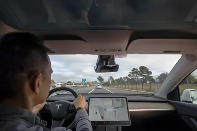 Inifrån en Tesla på motorväg. Föraren håller i ratten, skärmen visar karta. Skylt "Exit 11".