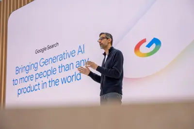 Sundar Pichai på scen framför en skärm med texten "Google Search" och "Bringing Generative AI". Googles logotyp syns också.