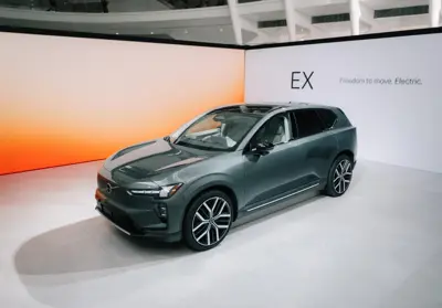 En grå Volvo EX60 står på en mässa framför en vägg med texten "EX Freedom to move. Electric.