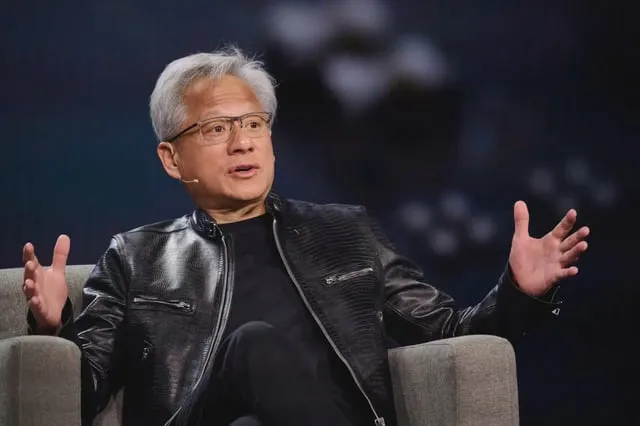 Jensen Huang, Nvidias chef, sitter i en grå fåtölj med utsträckta händer. Han bär glasögon och en svart skinnjacka.