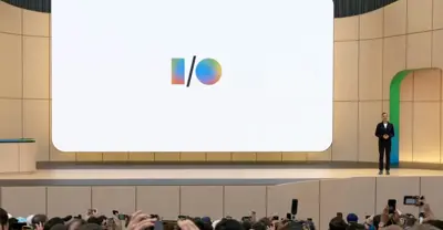 En man står på en scen framför en stor skärm med Google I/O-logotypen. Publiken fotograferar med mobiler.