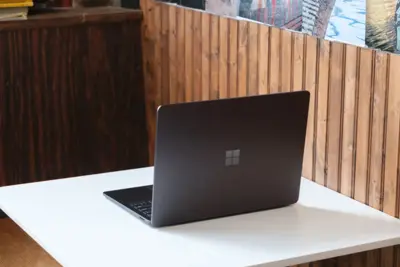 En grå Surface Laptop står på ett vitt bord med en träpanel i bakgrunden. Microsoft-loggan syns på locket.