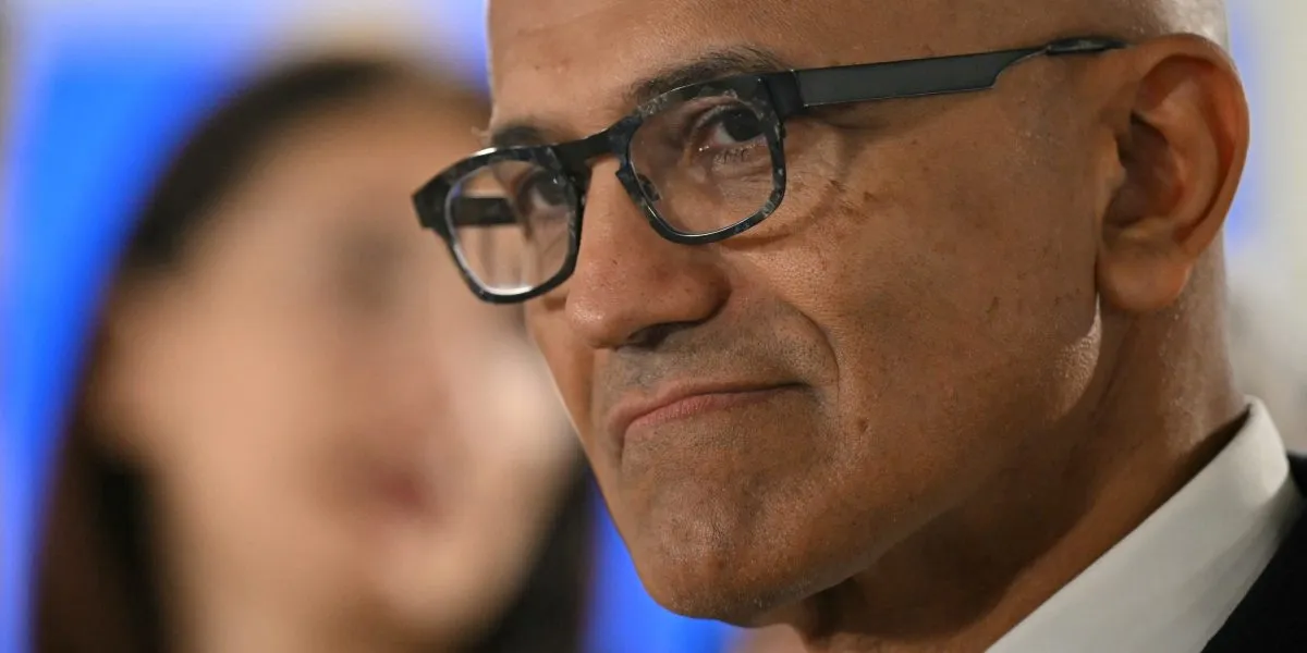 Närbild på Satya Nadella med glasögon, i profil. En suddig person syns i bakgrunden.