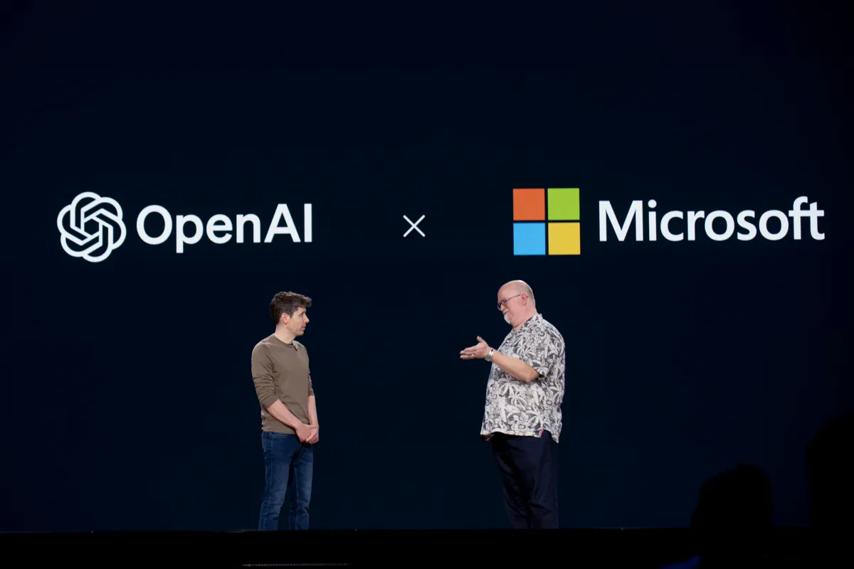 Två män står på en scen framför logotyperna för OpenAI och Microsoft.