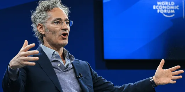 En man med glasögon och grått lockigt hår gestikulerar framför en blå bakgrund med "World Economic Forum".