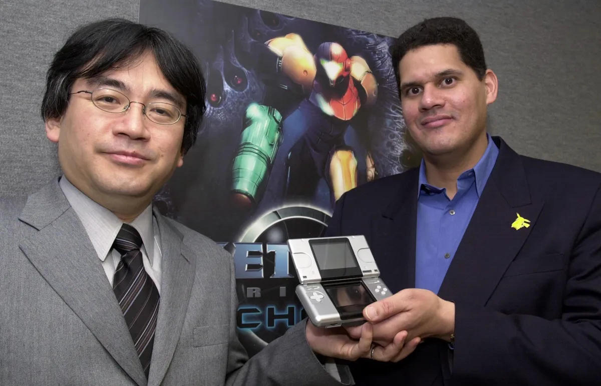 Shigeru Miyamoto och Reggie Fils-Aimé håller en Nintendo DS framför en Metroid Prime-affisch.