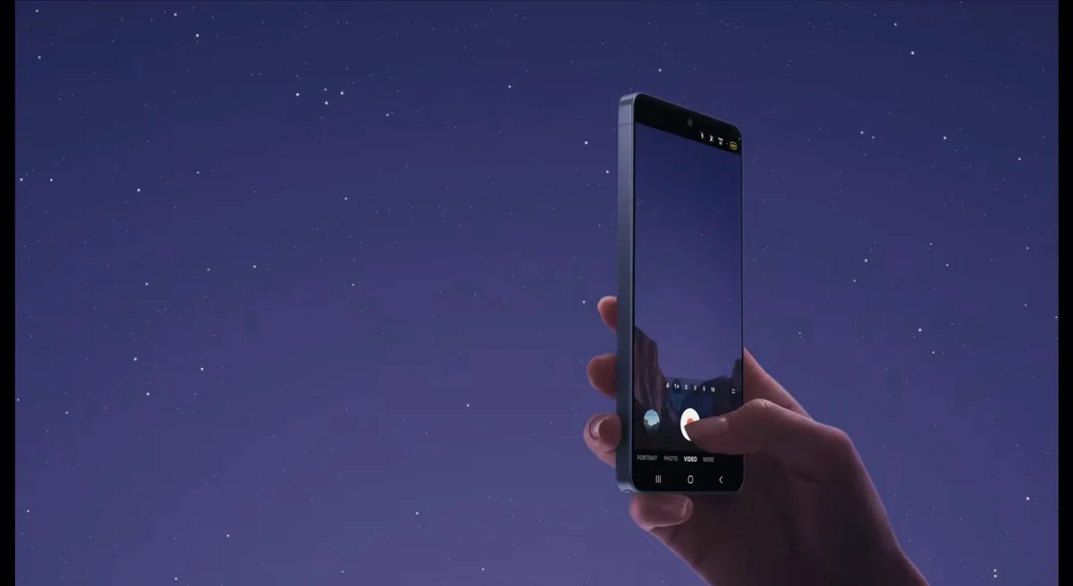 En hand håller en mobiltelefon mot en stjärnklar himmel. Telefonens skärm visar en kameraapp.