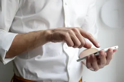 En person i vit skjorta håller en vit mobiltelefon och trycker på skärmen.