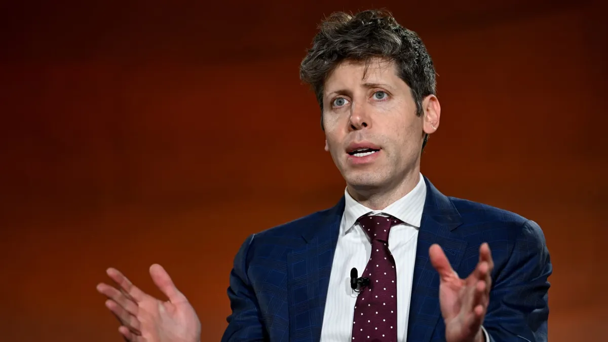 En man i kostym och slips gestikulerar framför en orange bakgrund.