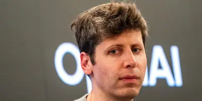 Närbild på en man med ljust hår framför en skärm med texten "OpenAI".