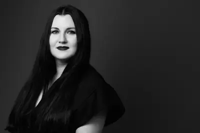 Svartvit porträttbild av kvinna med långt, mörkt hår och mörka läppar. Hon bär en mörk klänning.