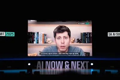 En man syns på en skärm på en scen med texten "AI NOW & NEXT". Text om AI syns också.