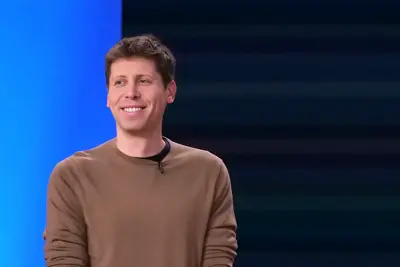 En leende Sam Altman i brun tröja, mot en blå bakgrund.