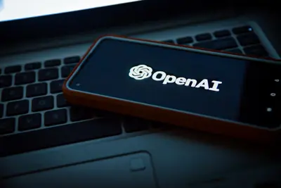 En mobiltelefon med OpenAI:s logotyp ligger på ett tangentbord.