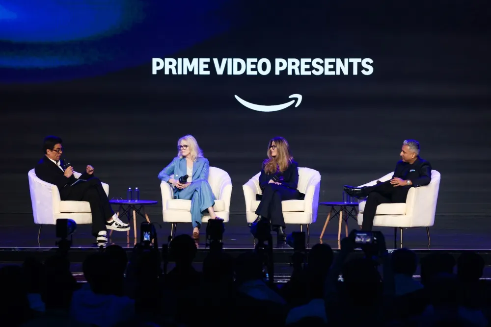 Fyra personer sitter på vita stolar på en scen framför en skärm med texten "Prime Video Presents". Publik i förgrunden.