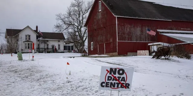 Vinterlandskap med röd lada, vitt hus och en skylt med texten "No Data Center". Amerikanska flaggor syns.