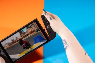 En person spelar Mario Kart på en Nintendo Switch med orange Joy-Cons. Bakgrunden är orange och blå.