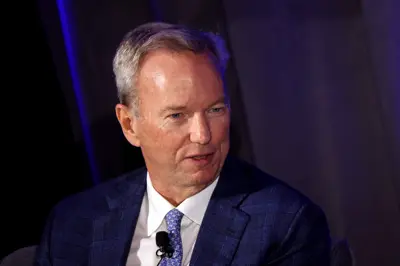 En man i kostym och slips, troligen Eric Schmidt, tittar åt sidan. Han har grått hår och en mikrofon fäst på skjortan.